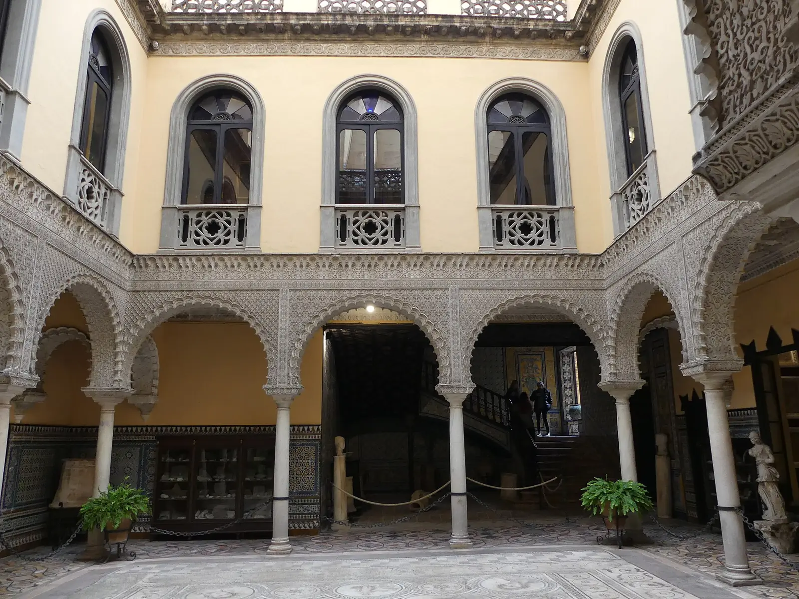 Vyřezávané štukové oblouky a žluté stěny kolem patia s mozaikovou podlahou v Palacio de la Condesa de Lebrija v Seville